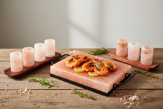 Himalayan salt cooking plate on black metal tray with grilled shrimp, set of 4 and set of 2 pink salt shot glasses on wooden stands — WoodenLandia