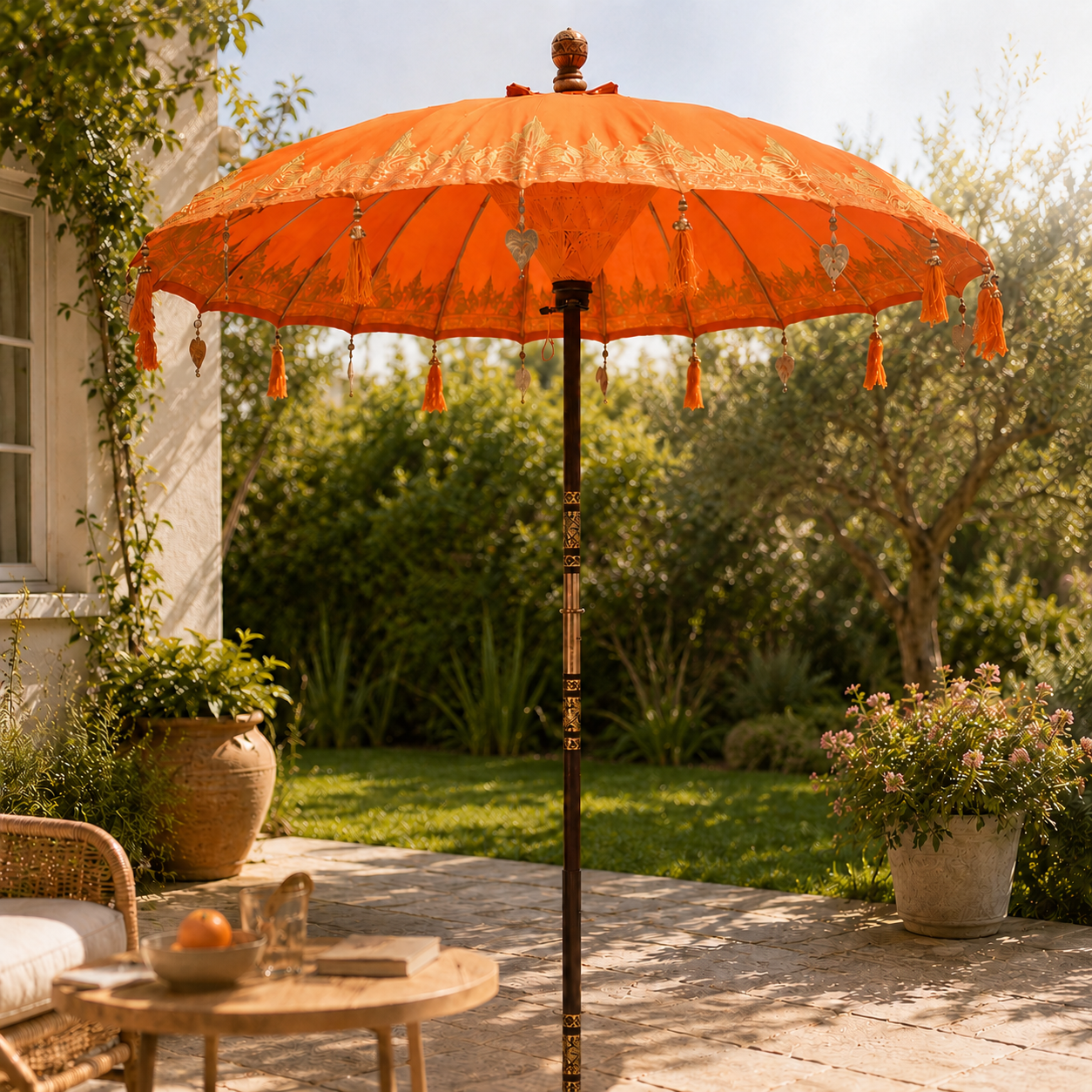 Orange Bali patio parasol with decorative gold detailing, tassels and wooden pole in outdoor setting